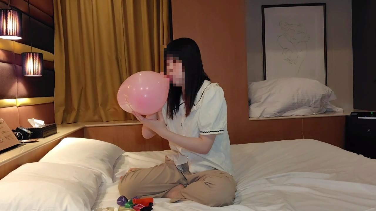 ベッドの上であぐらをかき、ピンクの風船を口でふくらませるひなた