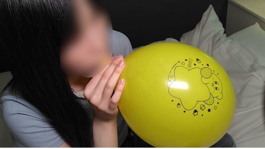 黄色いキャラクター柄の風船を口でふくらませるひなた