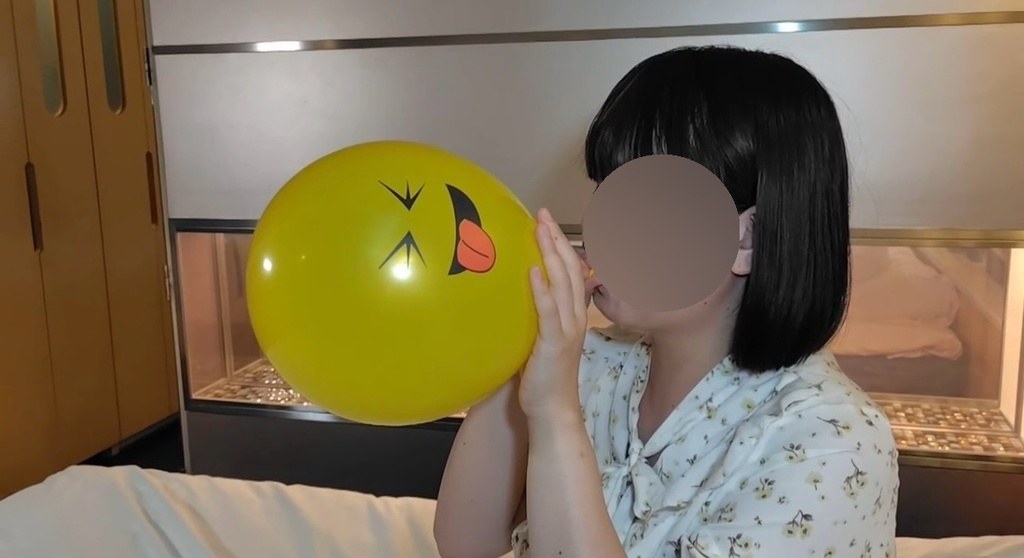 黄色い顔の絵の風船を口でふくらませるゲストモデルAさん