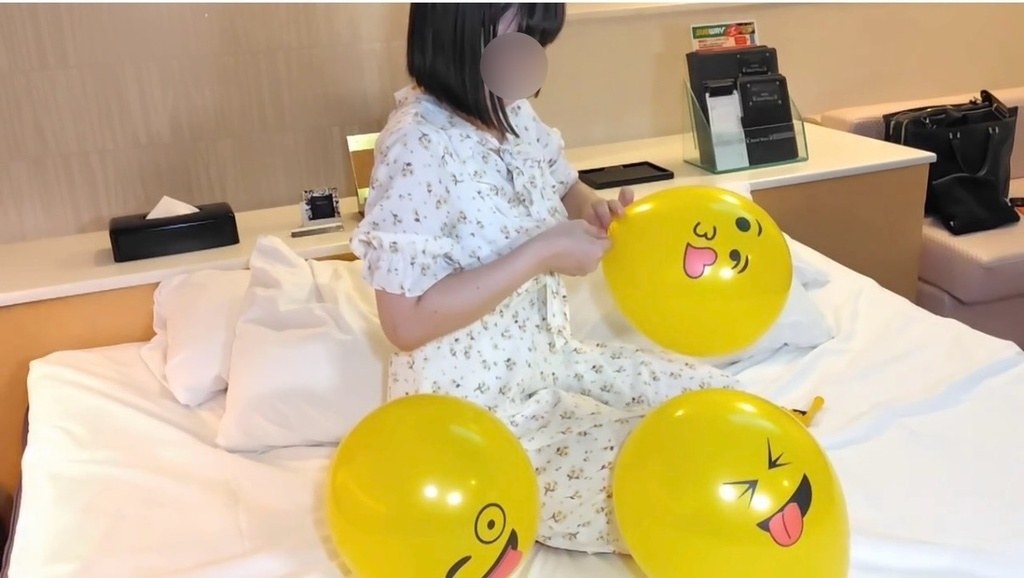 ふくらませた風船に囲まれて、次の風船の口を結ぶゲストモデルAさん