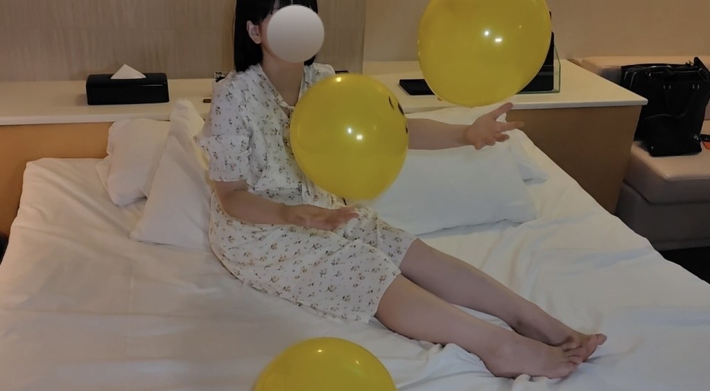 ベッドに座り、黄色い風船を放り上げて遊ぶゲストモデルAさん
