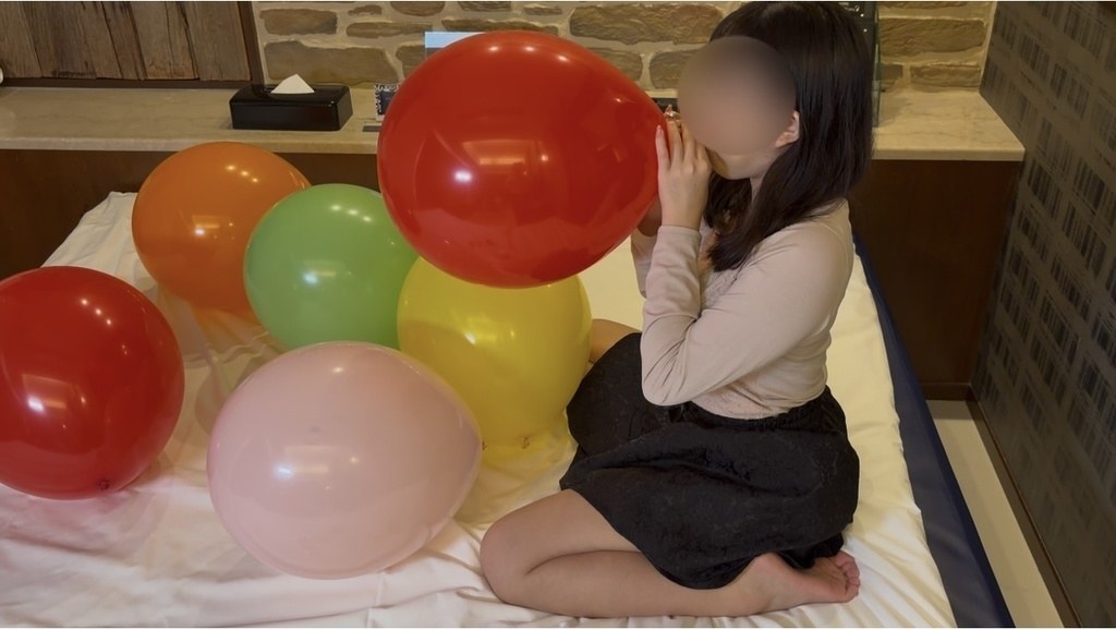色とりどりの風船に囲まれて赤い風船をふくらませるゲストモデルBさん