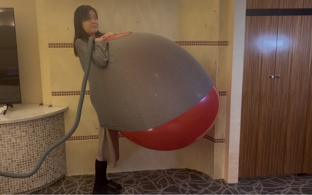 服の中で赤い巨大風船がふくらみ、前かがみになるゲストモデルDさん