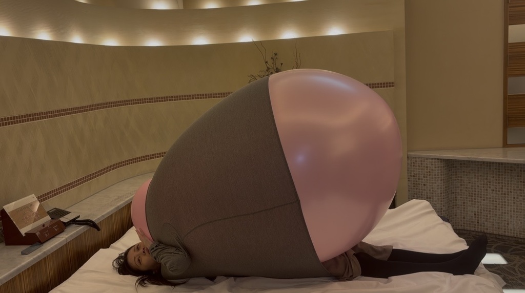 ベッドに横になり、服の中でピンクの巨大風船がふくらむゲストモデルDさん