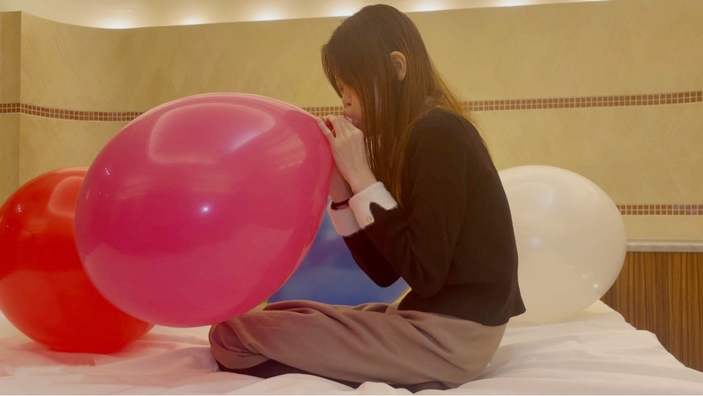 ピンクの風船を口で膨らませるゲストモデルDさん