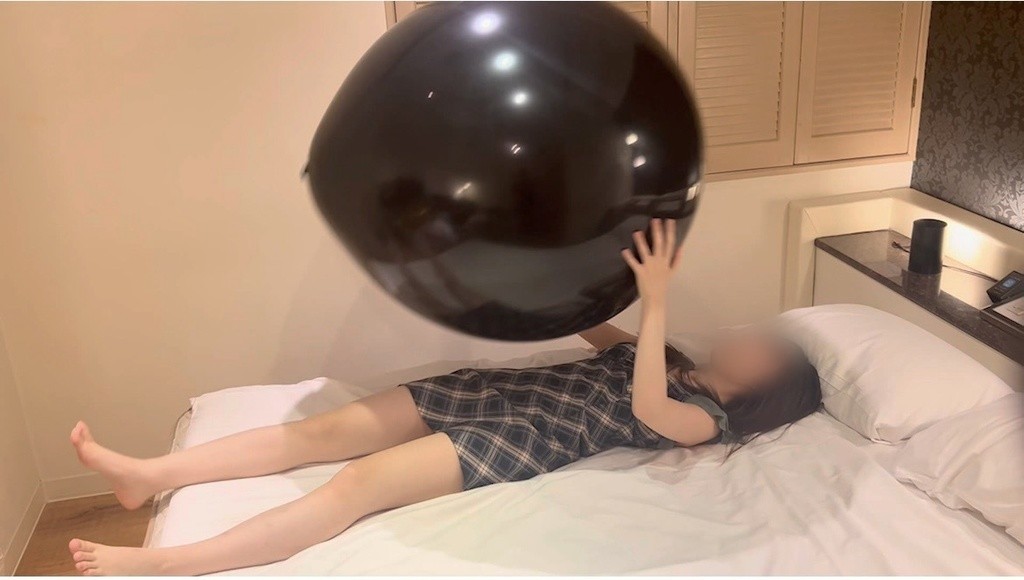 ベッドに寝転んで黒い巨大風船を持ち上げるひなた