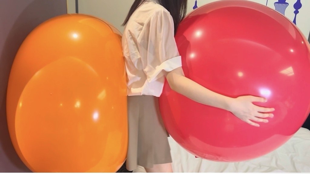 2つの巨大風船の間に立ってピンクの風船に抱きつくひなた