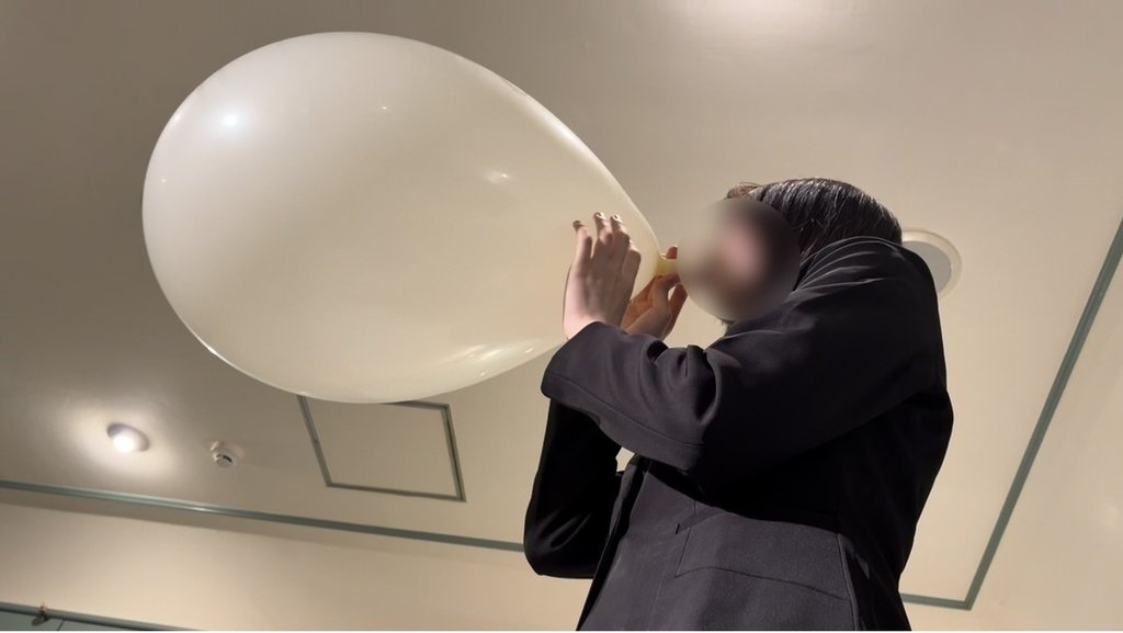 白い風船を口で膨らませるスーツ姿のひなた
