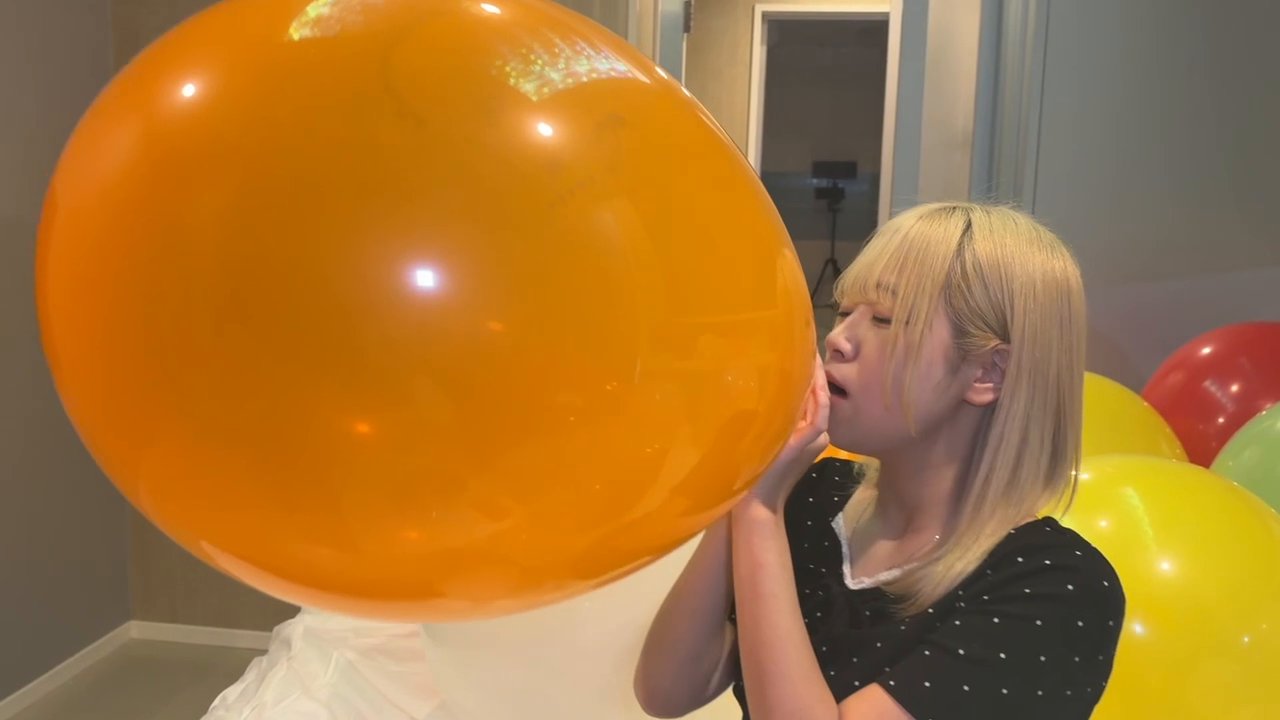 横のアングルから見た、顔よりずっと大きくなったオレンジの風船を膨らませる町田さん