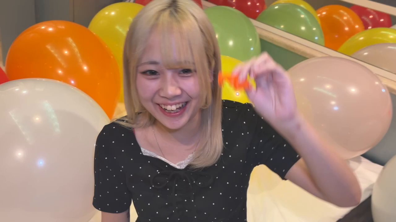 割れたオレンジの風船の破片を持って笑顔を見せる町田さん