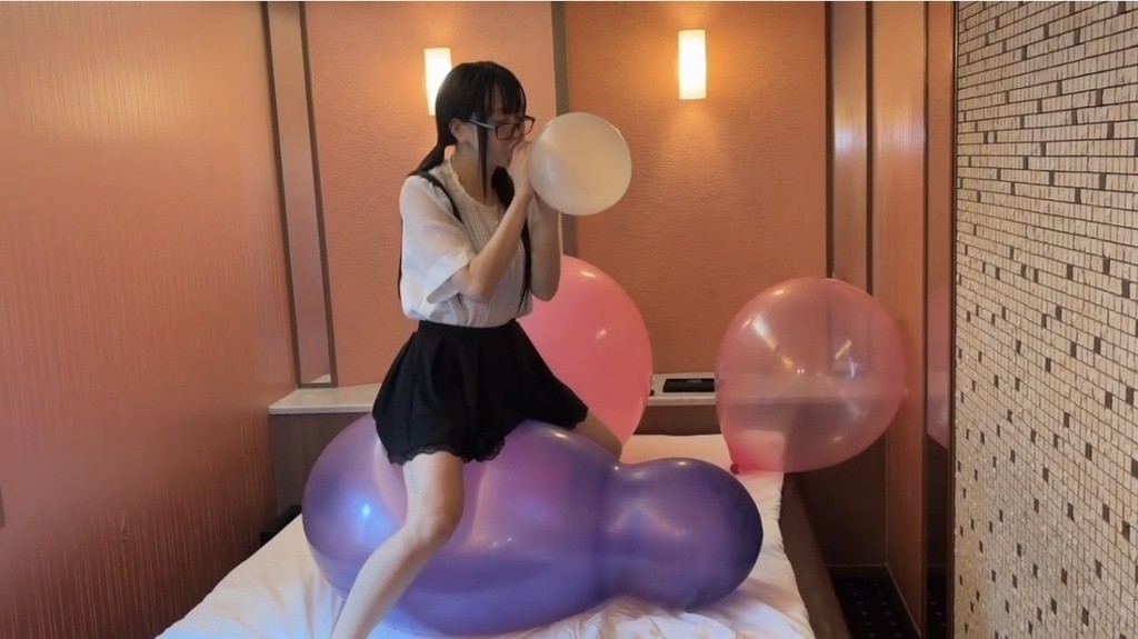 紫のひょうたん形の大きな風船にまたがり、透明な風船をふくらませる望月みうなさん
