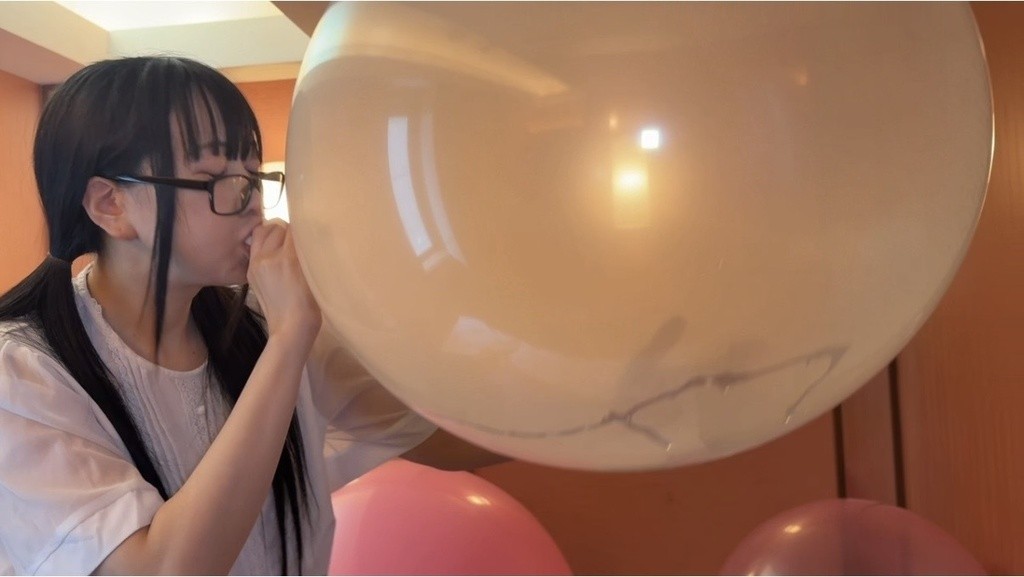 大きくふくらんだ透明な風船に、メガネ姿で息を吹き込む望月みうなさん