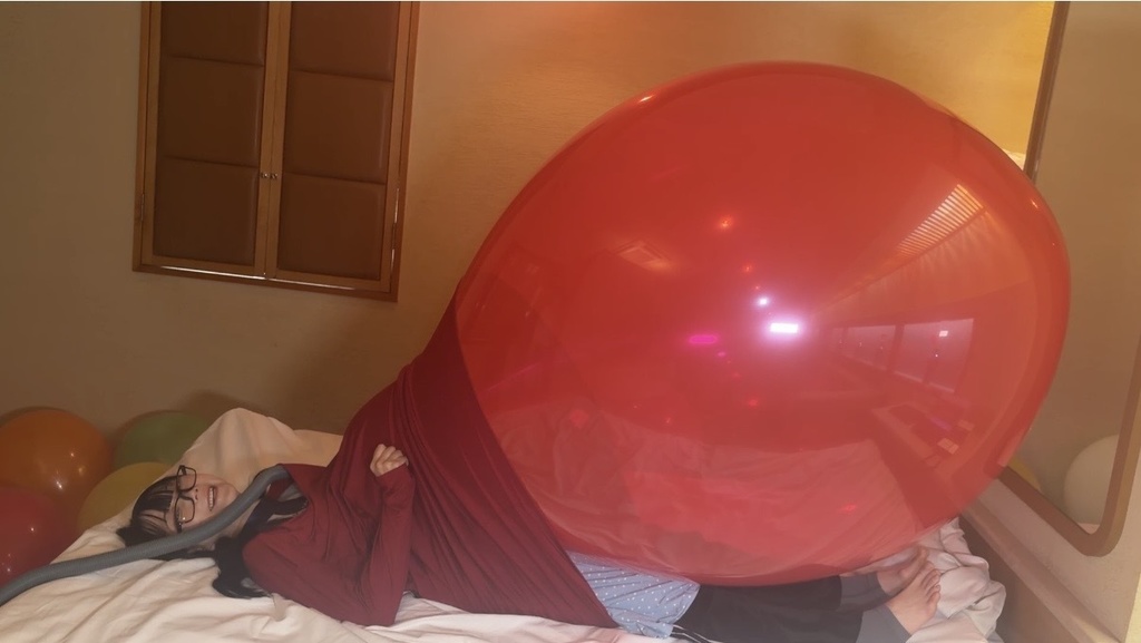 ベッドに横になり、服の中で大きくふくらんだ赤い風船に押される望月みうなさん