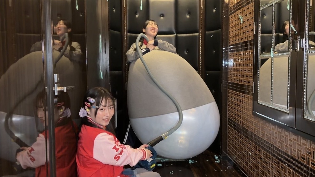 服の中の巨大風船をブロワーでふくらませる様子と、笑顔で見守る出演者